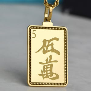 May include: Gold-colored rectangular pendant necklace with a rope chain. The pendant features the number "5" and Chinese characters. The pendant has a beaded border and is suspended from a gold-colored chain.
