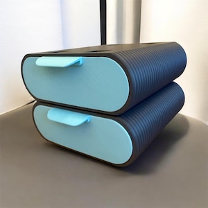 May include: A stack of two dark gray storage drawers with rounded ends and light blue drawer fronts. Each drawer features a small, protruding light blue handle centered on the front panel. The sides of the unit have a ribbed, textured surface.