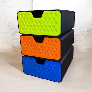 May include: Three-tiered storage containers stacked on top of each other. Each container is black with a colored front panel featuring a honeycomb pattern. The colors are green, orange, and blue. The containers have a recessed handle.