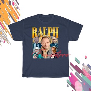 May include: Navy blue t-shirt with a gold-lettered "RALPH" design and multiple images of Ralph Fiennes. The portraits show the actor in different poses, creating a collage effect.