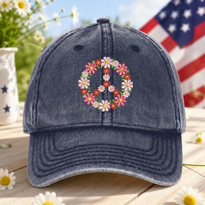 May include: A navy blue baseball cap with a floral peace sign embroidered on the front. The peace sign is made of pink, white, and yellow flowers. The cap is made of a soft, worn material.