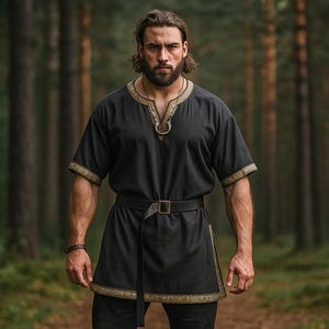 May include: Black tunic with gold trim and a belt. The short-sleeved top has a decorative neckline and is worn with black trousers. The image is set in a forest with tall trees in the background.