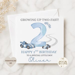 Puede incluir: Una tarjeta de cumplea&ntilde;os cuadrada con un gran n&uacute;mero dos en acuarela azul claro, dos coches de carreras azules, una bandera a cuadros y marcas de neum&aacute;ticos. El texto dice: GROWING UP TWO-FAST! HAPPY 2ND BIRTHDAY TO A SPECIAL LITTLE BOY Oliver.