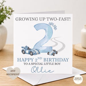 Puede incluir: Una tarjeta de felicitaci&oacute;n cuadrada con un n&uacute;mero dos grande en acuarela azul claro, dos coches de carreras azules y banderas a cuadros. El texto dice: GROWING UP TWO-FAST! HAPPY 2ND BIRTHDAY TO A SPECIAL LITTLE BOY, y el nombre Ollie en azul.