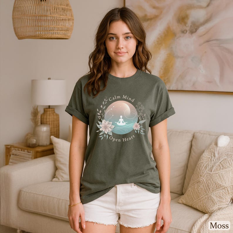 Puede incluir: Camiseta verde musgo con un dise&ntilde;o circular con las palabras "Calm Mind Open Heart". El dise&ntilde;o incluye una persona meditando, rodeada de flores y hojas, con un fondo rosa claro y azul.