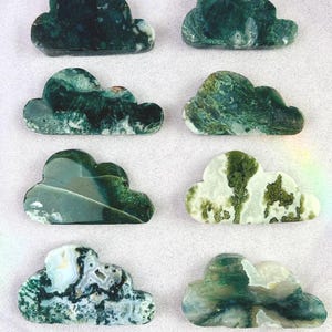 May include: Six cloud-shaped decorative stones. The stones are primarily green with white and gray marbling. The cloud shapes vary in their patterns and color distribution, with some having more white or gray areas. The stones are arranged on a white surface.
