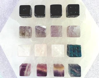 May include: A collection of sixteen dice in various colors and materials. The top row features four black dice. The second row has four purple and white dice. The third row has three clear and one teal dice. The bottom row has four dice with purple, yellow, and white patterns.