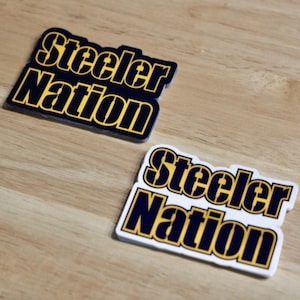 May include: Two stickers with the text "Steelers Nation" in black with yellow outlines. The top sticker is on a black background and the bottom sticker is on a white background.