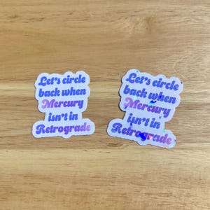 May include: Two white stickers with a holographic finish. The stickers have a purple and pink gradient and say "Let's circle back when Mercury isn't in retrograde".