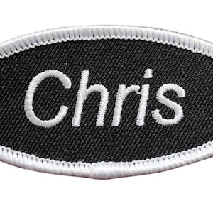 May include: An oval-shaped embroidered patch with the name "Chris" in white lettering on a black background. The patch is bordered with white stitching.