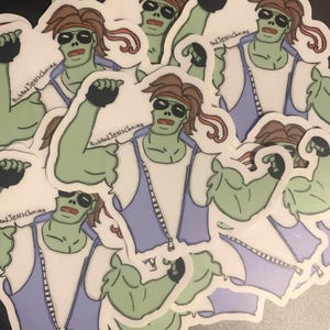 Puede incluir: Una pila de pegatinas con un personaje de zombie de dibujos animados con piel verde, cabello castaño y un chaleco morado. El personaje está flexionando su bíceps y tiene una expresión decidida. Las pegatinas tienen el texto "Rich and Jenschnainz" impreso en ellas.