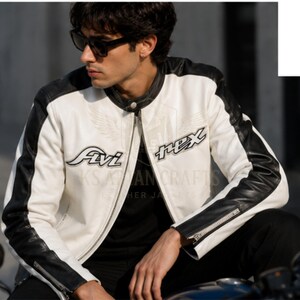 May include: A white and black leather motorcycle jacket with the text "Fivi" and "Rex" on the front. The jacket has black accents on the shoulders and sleeves, and a zipper closure. The jacket is worn by a person wearing sunglasses.