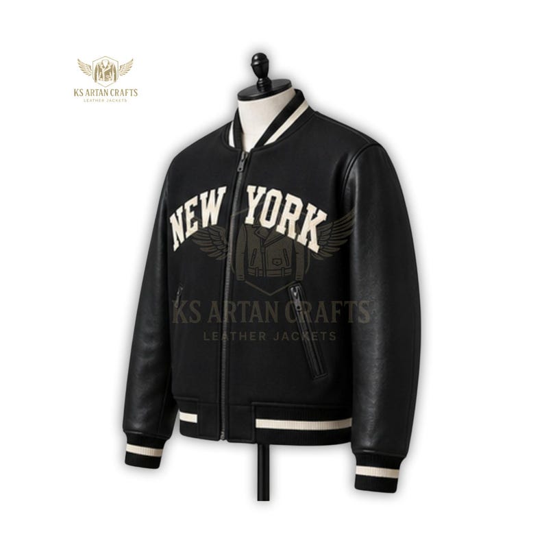 May include: A black leather bomber jacket with the text "NEW YORK" in white block letters across the chest. The jacket has white stripes on the collar, cuffs, and hem. The jacket is displayed on a mannequin.