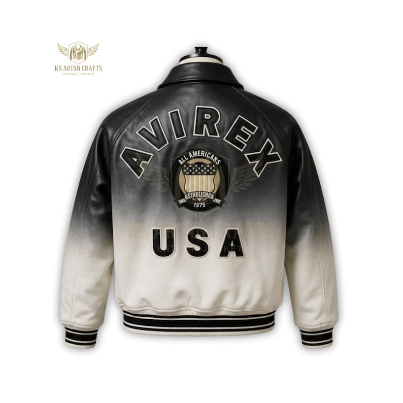 K&ouml;nnte beinhalten: Schwarz-wei&szlig;e Lederjacke mit dem Text "AVIREX" und "USA" auf dem R&uuml;cken. Die Jacke hat einen klassischen Bomberstil mit geripptem Kragen und B&uuml;ndchen. Die Jacke hat ein Farbverlauf-Design, das von Schwarz oben nach Wei&szlig; unten &uuml;bergeht.