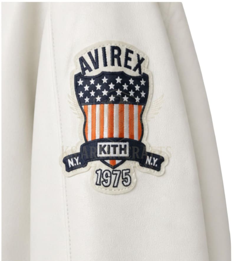 May include: Close-up of a white leather jacket featuring a patch with the text "AVIREX" above a design of stars and stripes. Below the design is the text "KITH" and "1975". The jacket has a classic design.