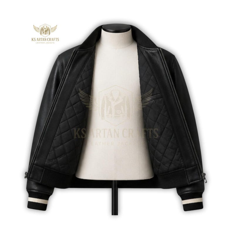 May include: Black leather bomber jacket with a quilted interior, displayed on a mannequin. The jacket features a ribbed collar, cuffs with white stripes, and a zipper closure. The interior lining is black and diamond-stitched.