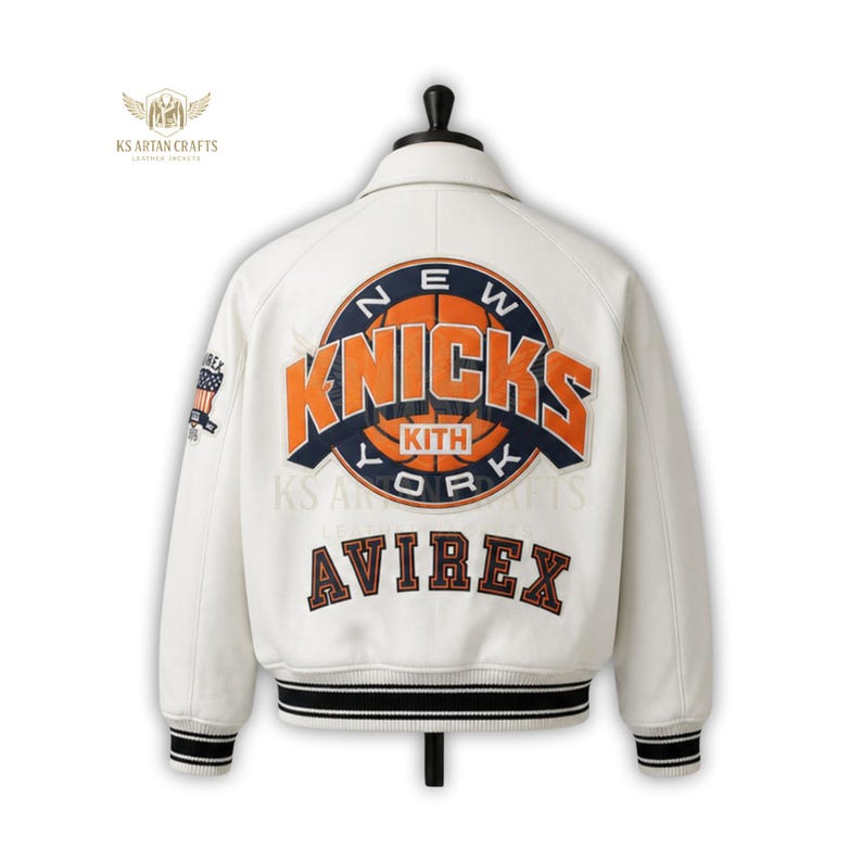 May include: Cream-colored varsity jacket with the New York Knicks logo in orange and navy blue on the back. The jacket features the Avirex brand name and a striped black and white ribbed hem. A small American flag patch is on the sleeve.
