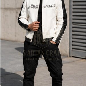May include: A white and black leather jacket with the text "Avi Rex U.S.A." and "Avi Rex" on the front. The jacket has black sleeves and a black collar. The person is wearing black pants and black boots.