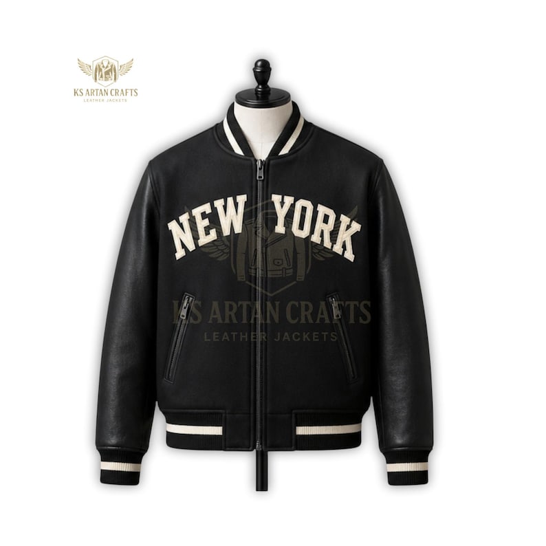 May include: Black leather varsity jacket with the text "NEW YORK" in white block letters. The jacket has a white collar, cuffs, and waistband with black stripes. The jacket is zipped up and has two front pockets.