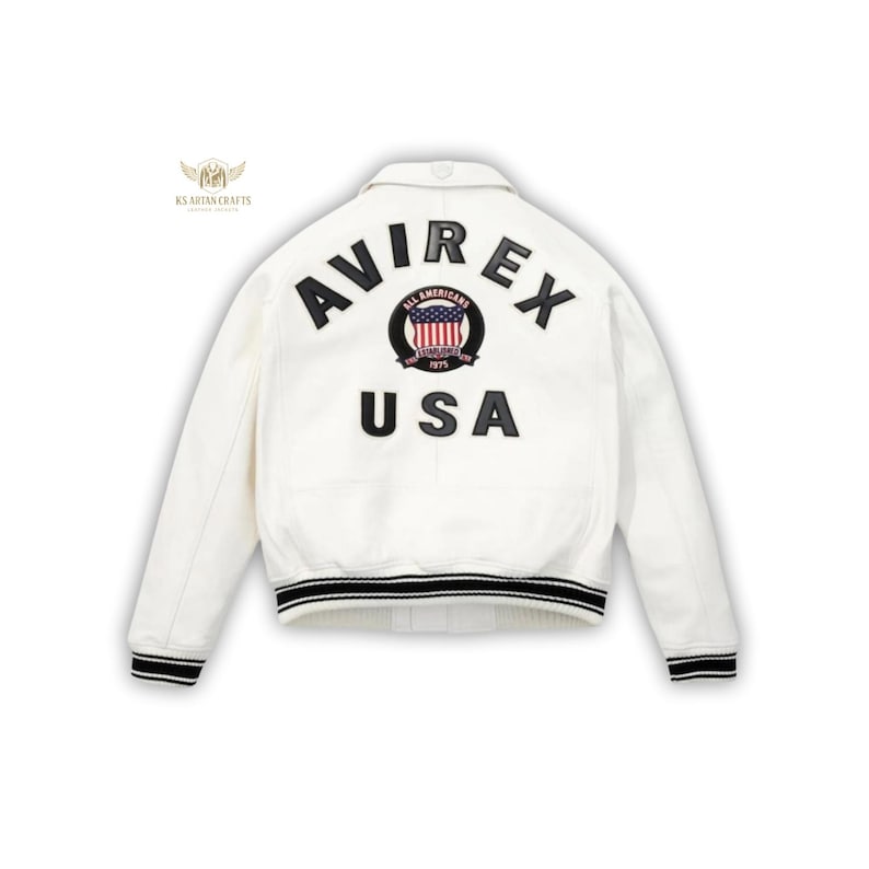 May include: White jacket with the word "AVIREX" arched across the back in black lettering, above "USA". A circular emblem with the American flag is centered between the words. The jacket has black and white striped trim on the cuffs and hem.