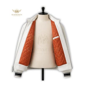 May include: White leather jacket with a ribbed collar, cuffs, and hem. The jacket features a zipper closure and a quilted orange lining. The cuffs have black and white stripes. The jacket is displayed on a mannequin. The brand logo is visible on the upper left.