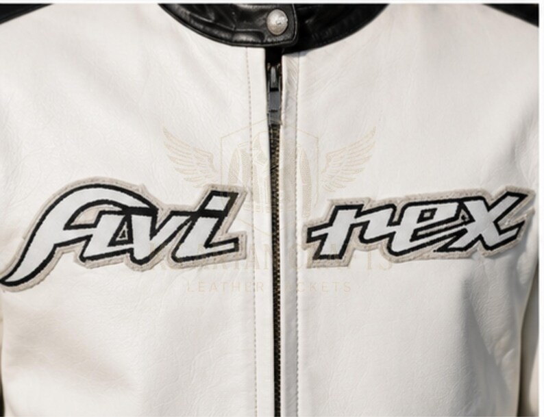 May include: Close-up of a white leather jacket with black accents on the collar and shoulders. The jacket features the embroidered text "Avi Nex" in black and white, with a gray outline. A silver zipper runs down the center.