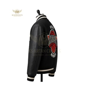 May include: Black leather jacket with white and black striped collar and cuffs. Features a red and white basketball graphic with the word "Knights" and the brand name "Kith". The jacket is displayed on a mannequin.