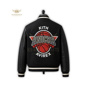 May include: Black varsity jacket with leather sleeves and a white and black striped collar and cuffs. The back features a large circular patch with the text "KITH" above a basketball and the word "KNICKS". The brand name "AVIREX" is below the basketball.