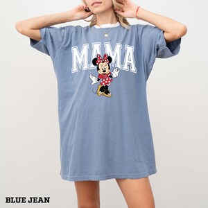 May include: Blue jean colored t-shirt with the word "MAMA" in white block letters. A cartoon Minnie Mouse is in the center, wearing a red polka dot bow and dress. The text "BLUE JEAN" is at the bottom.