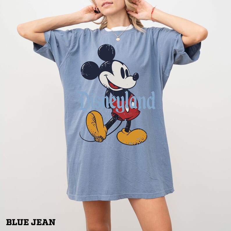 K&ouml;nnte beinhalten: Blaues Jeans-T-Shirt mit einem Vintage-Mickey-Mouse-Motiv und dem Wort "neyland" in Hellblau. Das Shirt hat eine lockere Passform und einen wei&szlig;en Ausschnitt. Der Text "BLUE JEAN" ist unten aufgedruckt.
