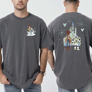 K&ouml;nnte beinhalten: Dunkelgraues T-Shirt mit einem Cartoon-Design von Woody und Buzz Lightyear. Die Vorderseite zeigt Woody und Buzz in einer Teetasse, und die R&uuml;ckseite hat ein Schloss und Feuerwerk. Das T-Shirt ist aus weichem Material.