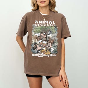 May include: Brown t-shirt featuring a graphic of Disney characters, including Mickey and Minnie Mouse, Donald Duck, and Goofy, with the text "ANIMAL KINGDOM" and "Walt Disney World" in white.