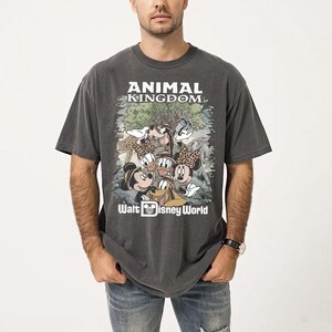 May include: Dark gray t-shirt featuring the text "ANIMAL KINGDOM" and "Walt Disney World." The shirt has a graphic of Mickey Mouse, Minnie Mouse, Donald Duck, Goofy, and other characters. The shirt is worn by a person.