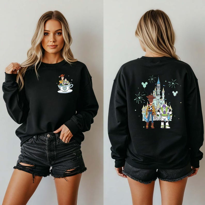 K&ouml;nnte beinhalten: Schwarzes Sweatshirt mit einem Cartoon-Design von Toy Story-Charakteren in einer Teetasse auf der Vorderseite und einem Schloss mit Charakteren auf der R&uuml;ckseite. Das Sweatshirt hat lange &Auml;rmel und einen Rundhalsausschnitt.