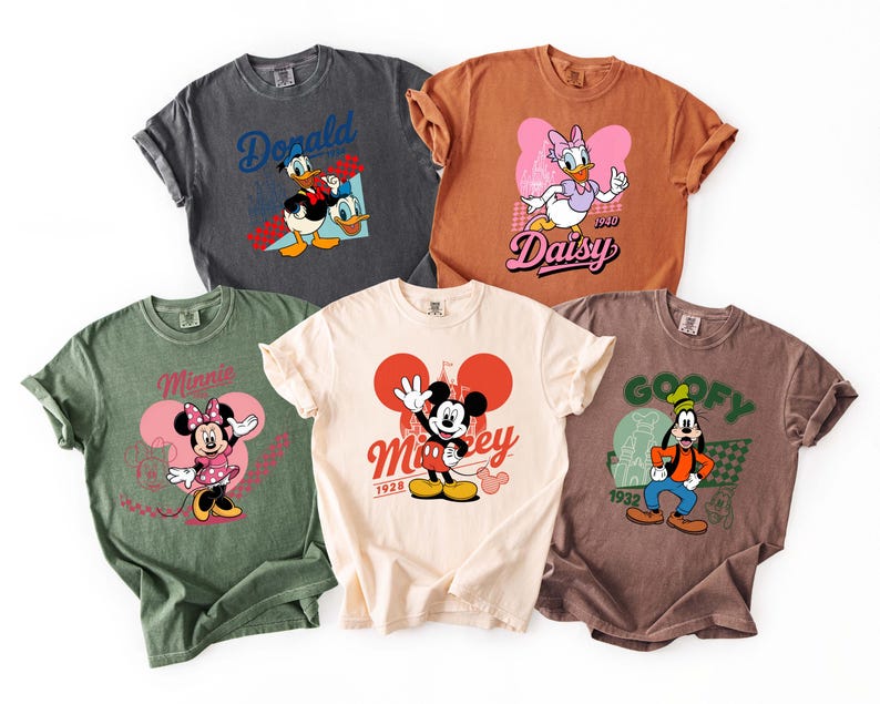 Może przedstawiać: Pięć kolorowych koszulek z postaciami Disneya. Koszulki są w r&oacute;żnych kolorach, w tym szarym, brązowym i zielonym. Każda koszulka ma inną grafikę postaci, taką jak Kaczor Donald, Daisy, Myszka Minnie, Myszka Miki i Goofy.