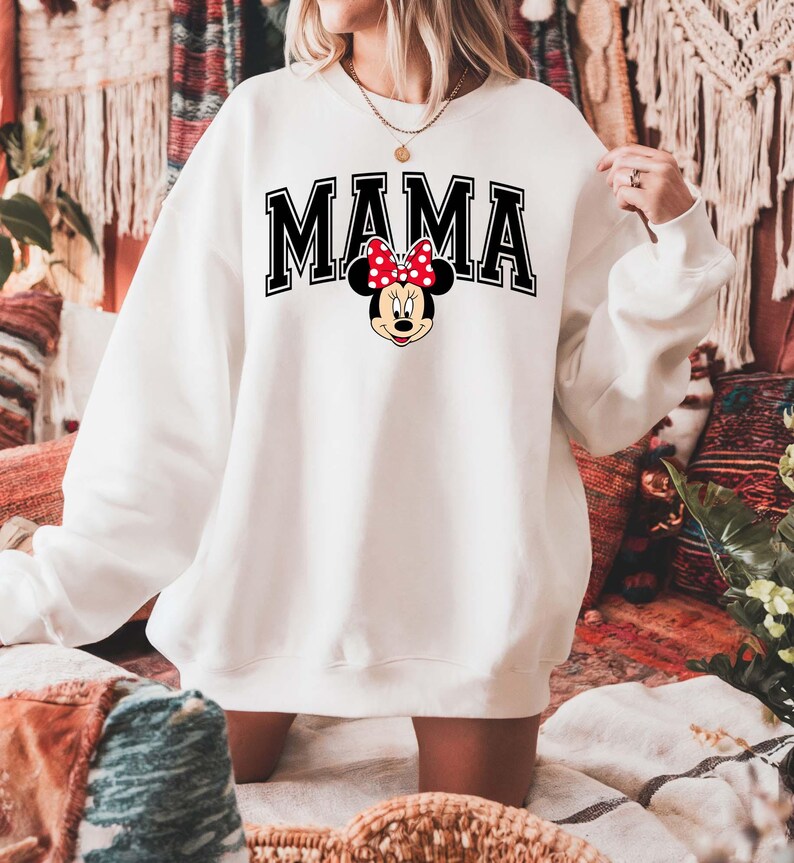 May include: White sweatshirt with the word "MAMA" in black block letters with a black outline. A Minnie Mouse graphic with a red bow and polka dots is centered below the word "MAMA".