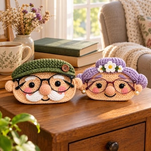 May include: Two crocheted pouches shaped like elderly faces. The left pouch has a green cap, brown button, white moustache, and black glasses. The right pouch has purple hair, white flower accents, pearl earrings, and thin-rimmed glasses.