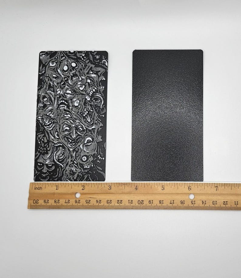 May include: Two rectangular pieces of black material, one with a white and gray pattern of faces and the other solid black. A ruler is placed below the two pieces of material.