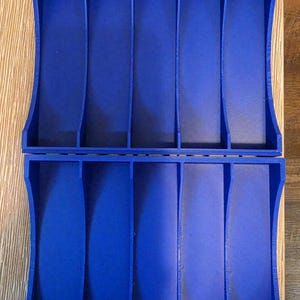 Peut inclure: Deux organisateurs en plastique bleu assortis, chacun avec six compartiments verticaux. Les organisateurs ont des c&ocirc;t&eacute;s incurv&eacute;s et un int&eacute;rieur textur&eacute;. Ils sont probablement con&ccedil;us pour ranger de petits objets.