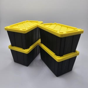 May include: Four black storage bins with yellow lids are stacked in a group. The bins are rectangular with a textured surface. The yellow lids have a grid-like pattern. The bins are designed for storage and organization.