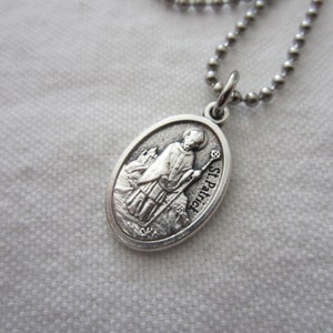 May include: Silver-toned oval pendant necklace featuring a detailed relief of St. Patrick holding a staff, with the inscription "St. Patrick." The pendant hangs from a delicate ball chain, creating a religious or spiritual accessory.