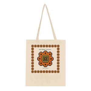 Op de afbeelding: Een beige canvas draagtas met een centraal geometrisch, bloemachtig motief in oranje, groen en zwart. Het ontwerp bevat een decoratieve rand van kleine herhalende bloempatronen en de tekst Deir Albalah- The moon en Arabisch schrift.