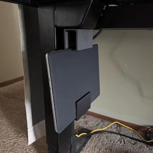 May include: Black tablet holder attached to a black adjustable desk frame. The holder is designed to securely hold a tablet, keeping it within easy reach. The setup is ideal for a home office or workspace.