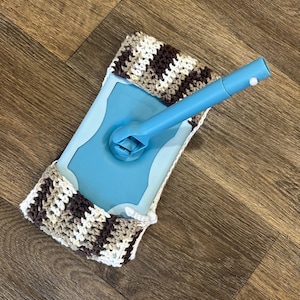 May include: A blue mop head with a brown and white crocheted cover. The mop head is attached to a blue plastic handle.