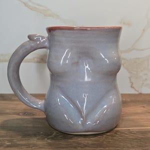 Könnte beinhalten: Ein Set aus drei Keramikbechern mit gesprenkelter, matter Oberfläche. Die Becher sind in den Farbtönen Creme, Hellgrau und Dunkelgrau gehalten. Jeder Becher hat ein schlichtes, minimalistisches Design, ideal für Kaffee oder Tee.