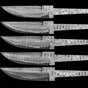 Puede incluir: Cinco hojas de cuchillo de acero de Damasco con mangos estampados se muestran sobre un fondo negro. Las hojas tienen una forma curva y un patrón arremolinado único. Los mangos tienen un aspecto de vetas de madera.