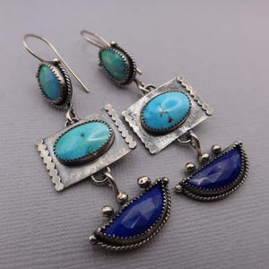 Pode incluir: Brincos de prata feitos à mão com pedras preciosas de turquesa e lápis-lazúli. Os brincos apresentam um design único com pedras de turquesa ovais, molduras de prata retangulares e detalhes de lápis-lazúli em forma de meia-lua.