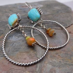 Pode incluir: Brincos de argola prateados com detalhes em pedras preciosas turquesa e laranja. Os brincos apresentam pedras turquesas quadradas, argolas de prata torcidas e pedras preciosas laranja penduradas.
