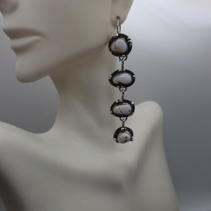 May include: Silver dangle earrings with four white oval stones. The stones have a black and white marbled pattern.