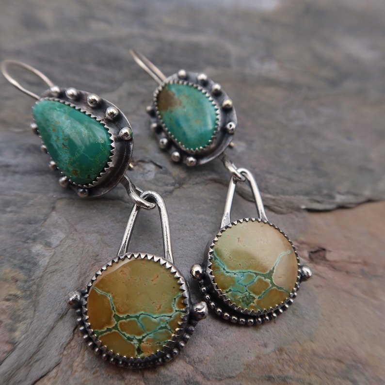 May include: Silver earrings with turquoise and tan-colored stones. The earrings have a teardrop-shaped turquoise stone at the top, connected to a circular tan stone with turquoise veining. The stones are set in a silver bezel with a beaded edge.